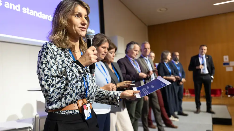 Woman presentering on stage. Her group is in the back.