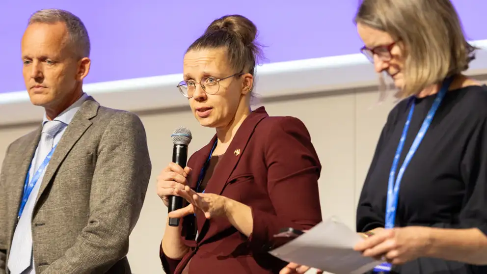 A man and two women presenting. One of the women are holding a microphone.