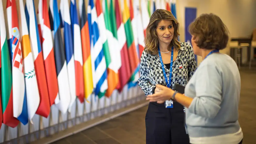Two women talking in front of flags.