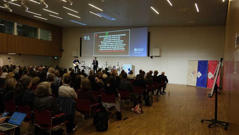 Band with two members are sining on stage. Audience in the front and power point in the back with song lyrics